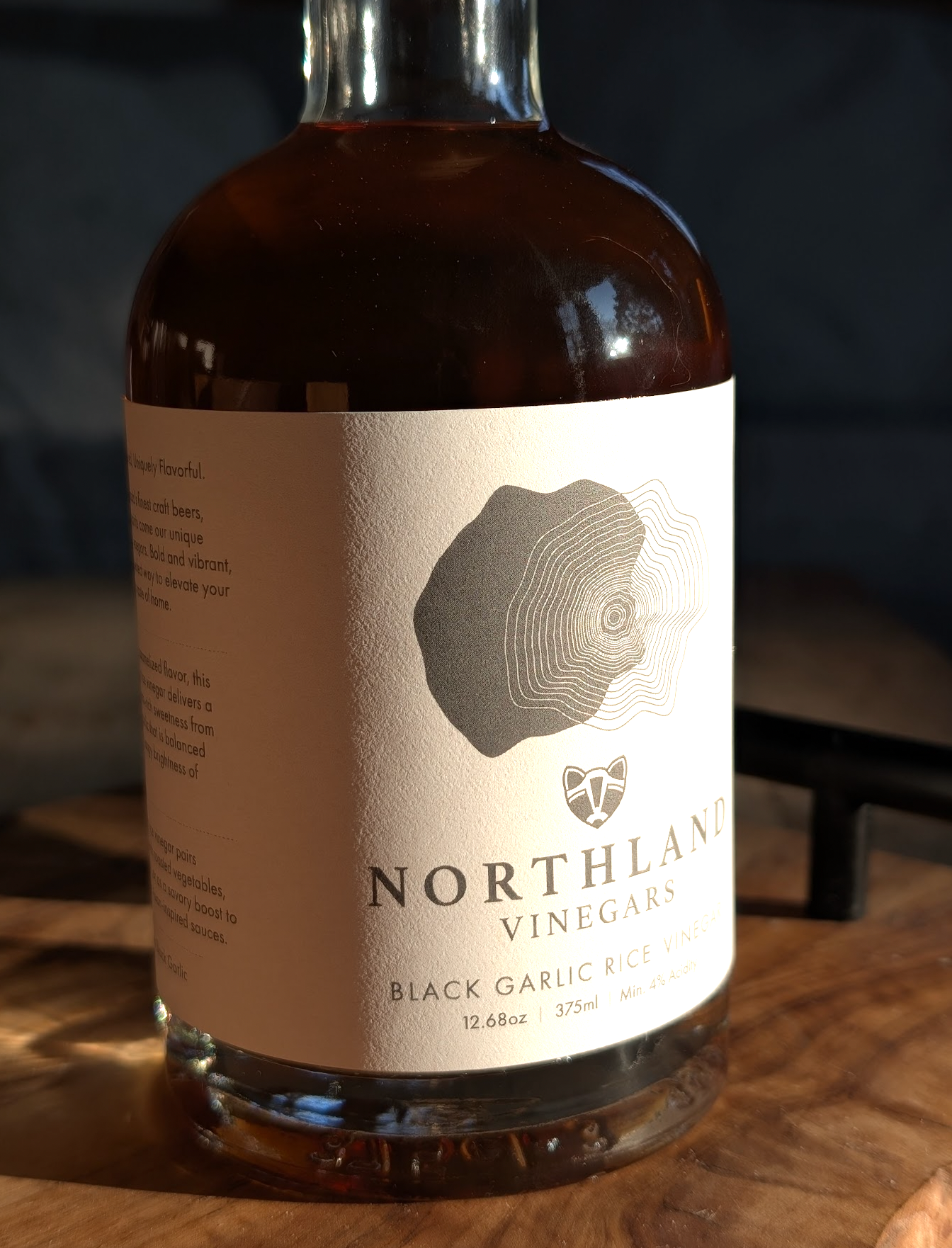 Bottle of Northland Vinegars Black Garlic Vinegar on a wooden surface with a blurred background
