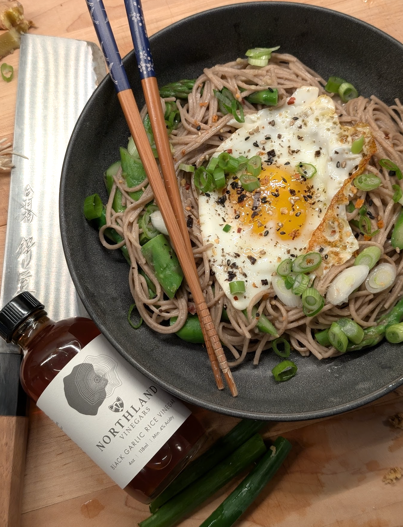 Bowl of soba noodles with a fried egg and green onions, accompanied by a bottle of Northland Vinegars Black Garlic Rice Vinegar