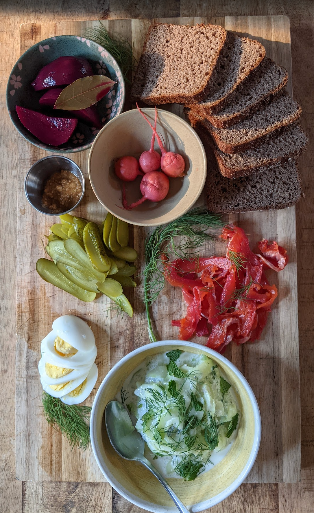 Assorted bread, pickles, radishes, and a bowl of salad on a wooden cutting board, utilizing our nordic Scandinavian celery aquavit vinegar