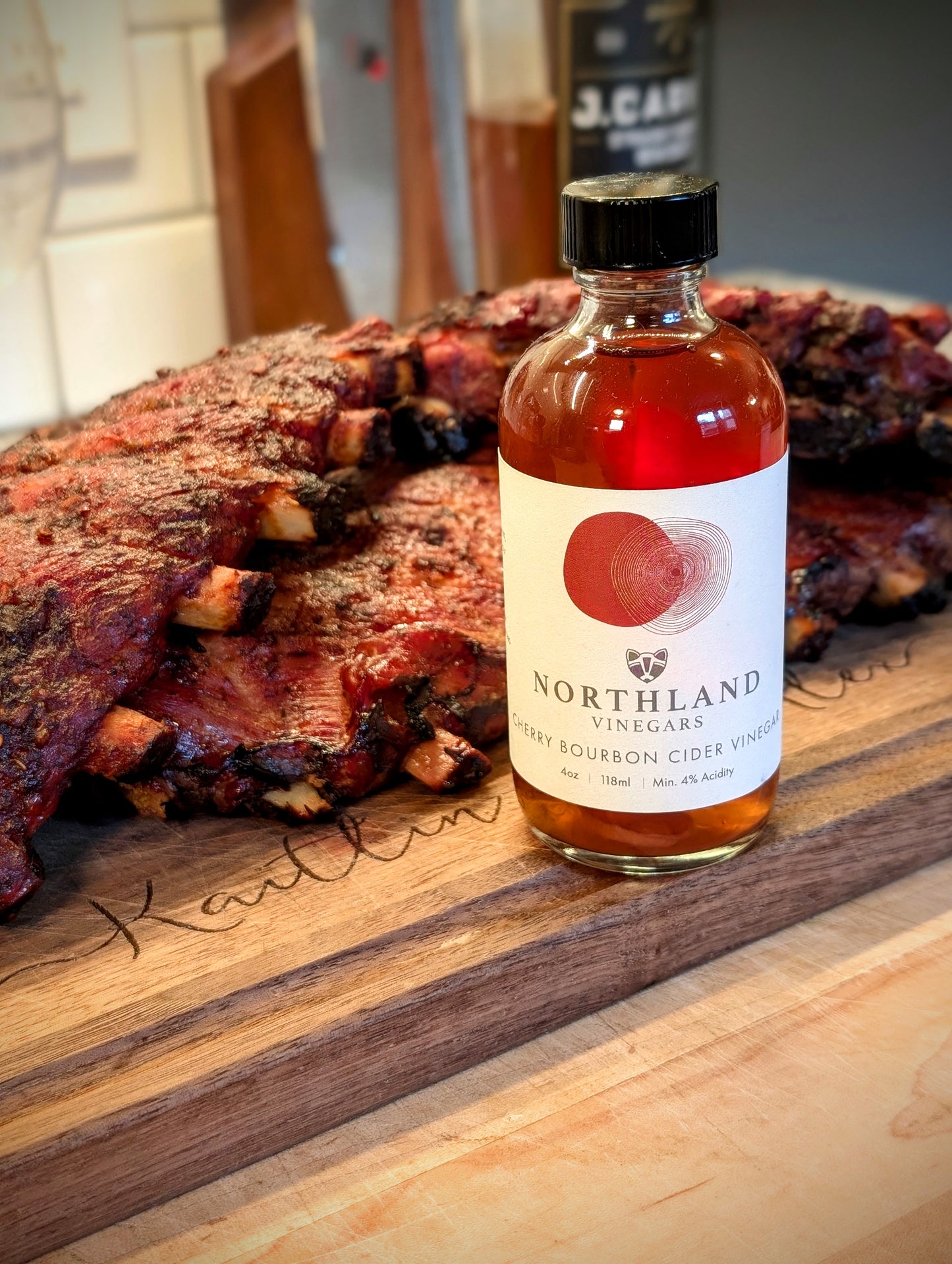 Bottle of Northland Vinegars cider vinegar on a wooden surface with ribs in the background
